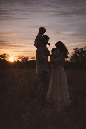 Silhouette of a family standing together against a vibrant sunset sky.