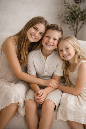 Three siblings in light colored clothing sitting close together on a couch.