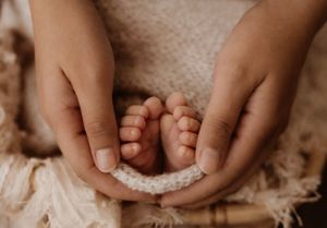 Tiny newborn baby feet cradled in gentle hands against a soft textured background.