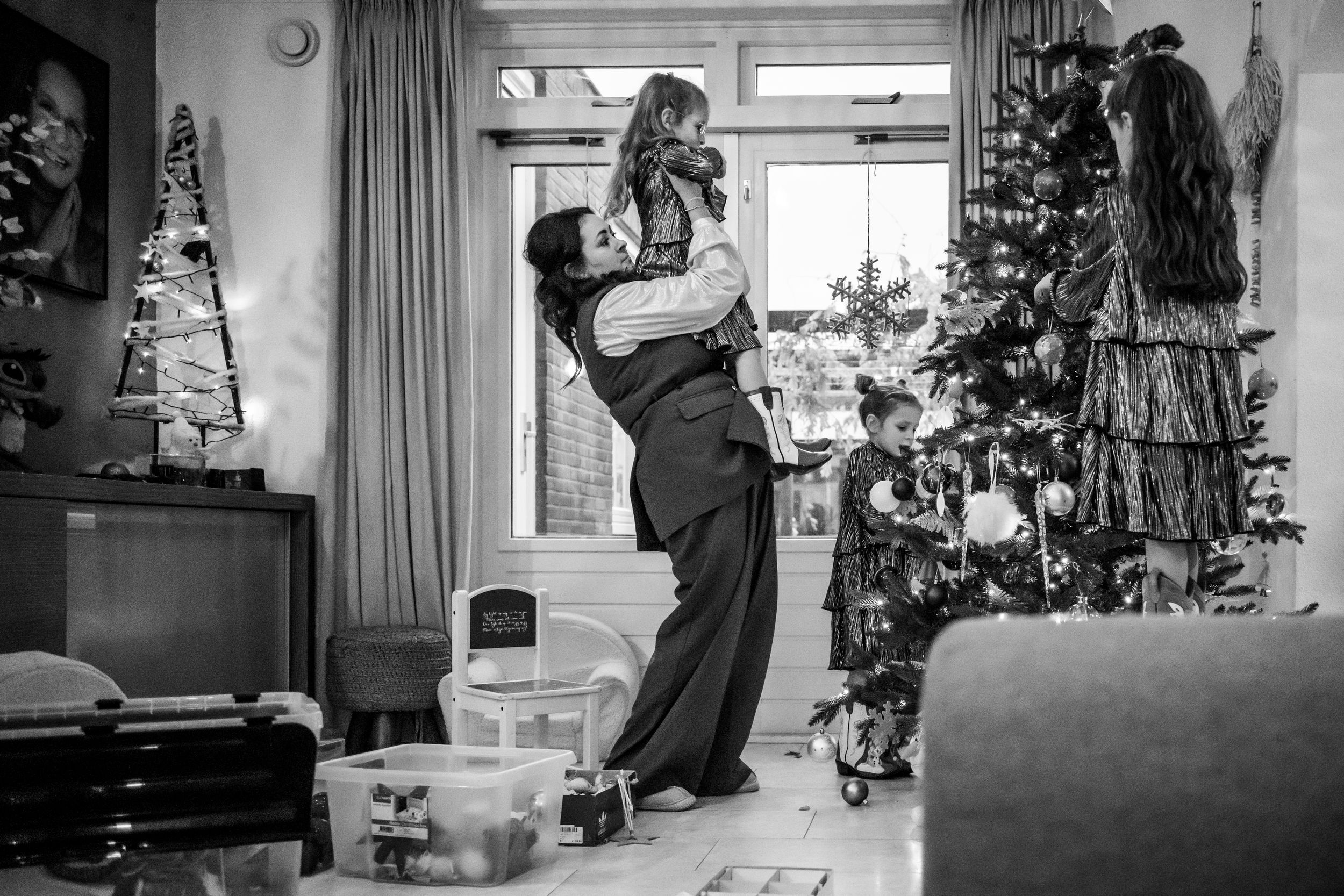 Black and white photo of parent joyfully lifting child in Christmas decorated living room.