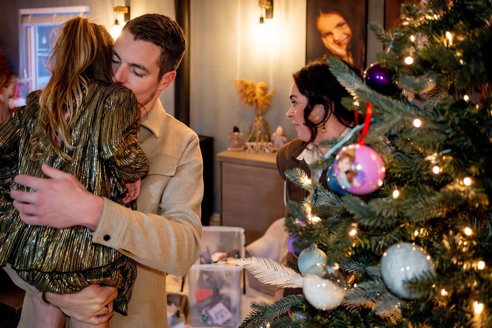 Two people hugging warmly near a decorated Christmas tree with ornaments during a holiday celebration.