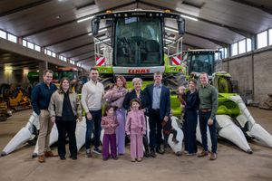 A group stands in front of large modern agricultural machinery including a CLAAS harvester in an indoor facility.
