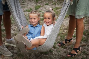 Children's feet dangle from hammocks in an outdoor setting while adults stand nearby.