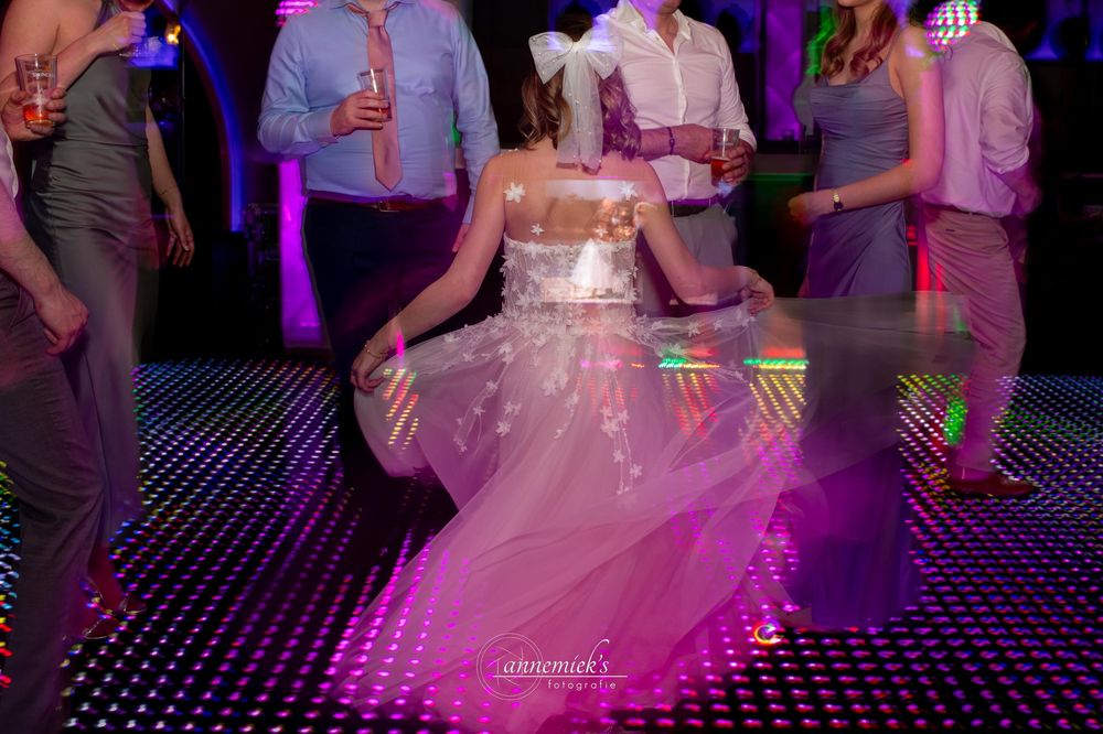 People dancing together on an illuminated dance floor with purple lighting and festive atmosphere at a celebration.