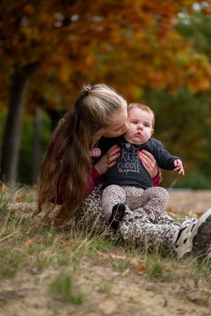 A tender moment captured outdoors with autumn foliage in the background on a grassy hillside.