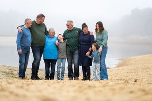 A family group stands together on a misty beach with waves and fog in the background.