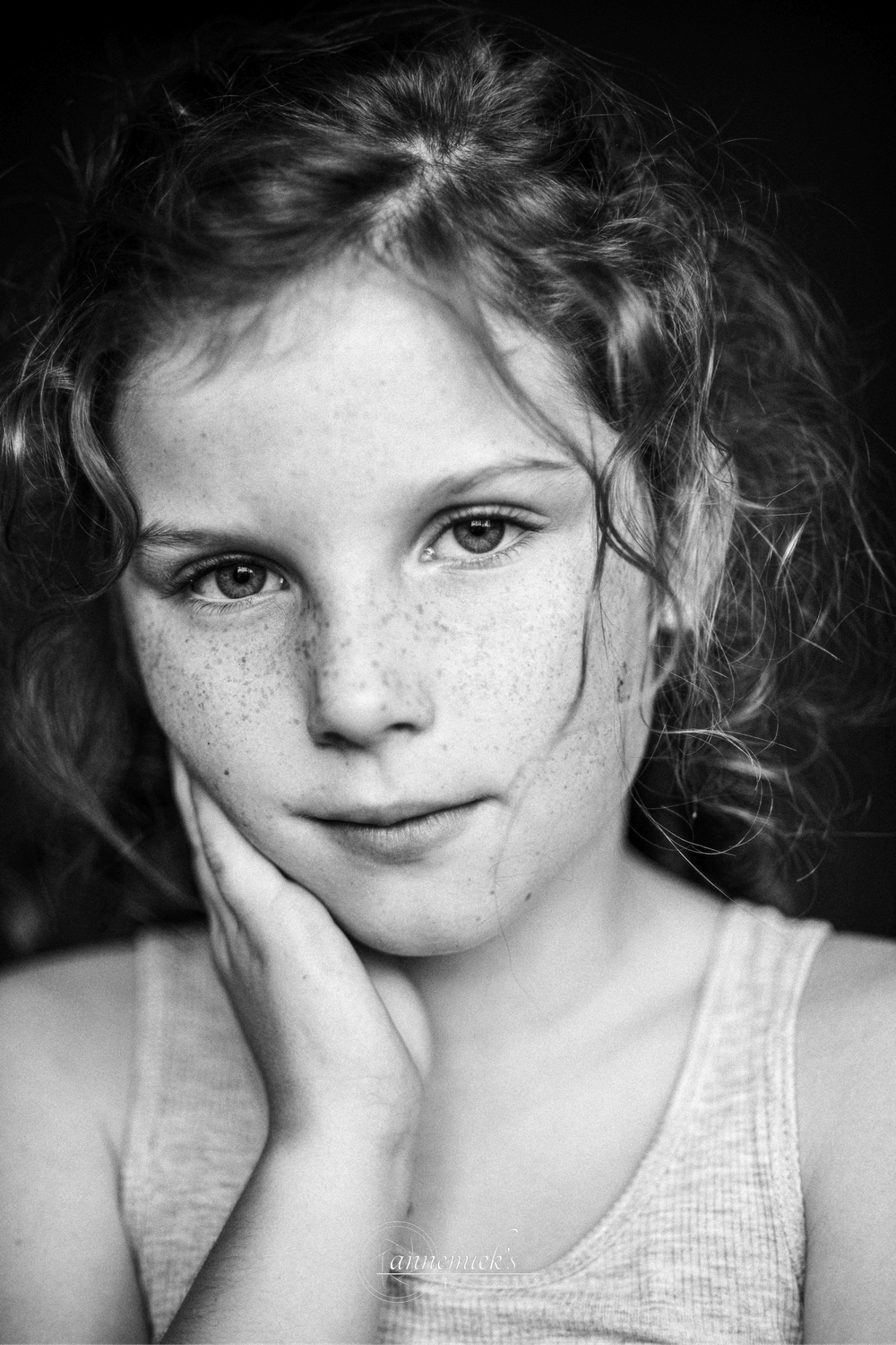 A black and white portrait showing freckles and curly hair against a dark background.