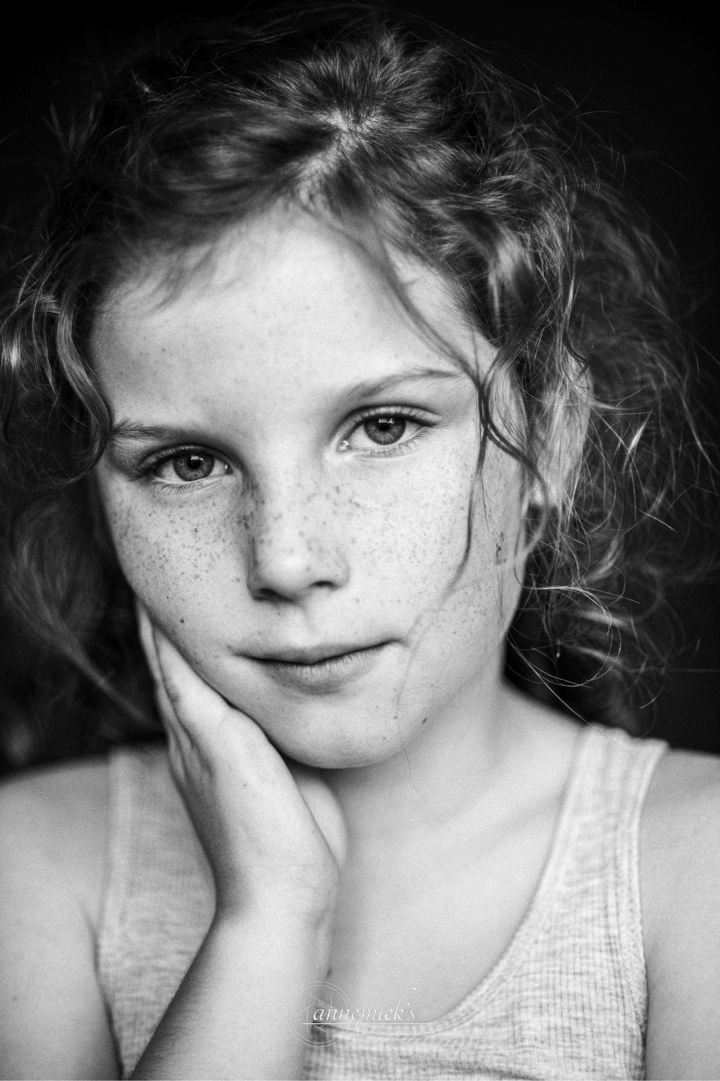 A black and white portrait showing freckles and curly hair against a dark background.