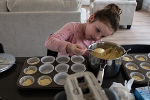 A person carefully pours batter into muffin tins while baking in a home kitchen.