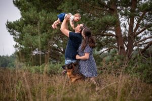A joyful family moment outdoors with their German Shepherd dog watching nearby.