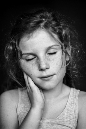 Black and white portrait of a young person with freckles and curly hair resting their eyes in a peaceful pose.