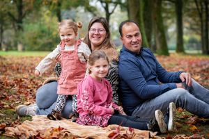 Family plays together in colorful autumn leaves during outdoor photo session in the park.