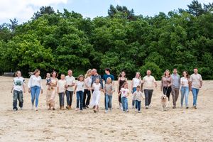 Group walking together on a sandy beach path surrounded by green trees on a sunny day.