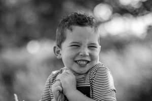 A sequence of black and white photos showing a child laughing and smiling in a striped shirt outdoors.