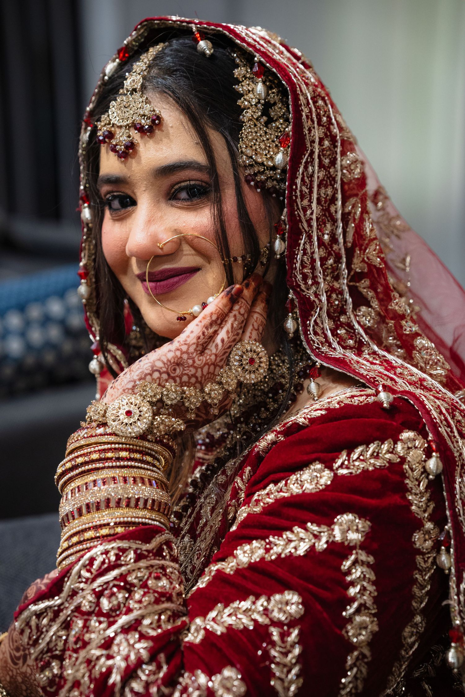Beautiful South Asian bride in ornate red bridal lehenga with gold embroidery, jewelry, and intricate mehndi henna.