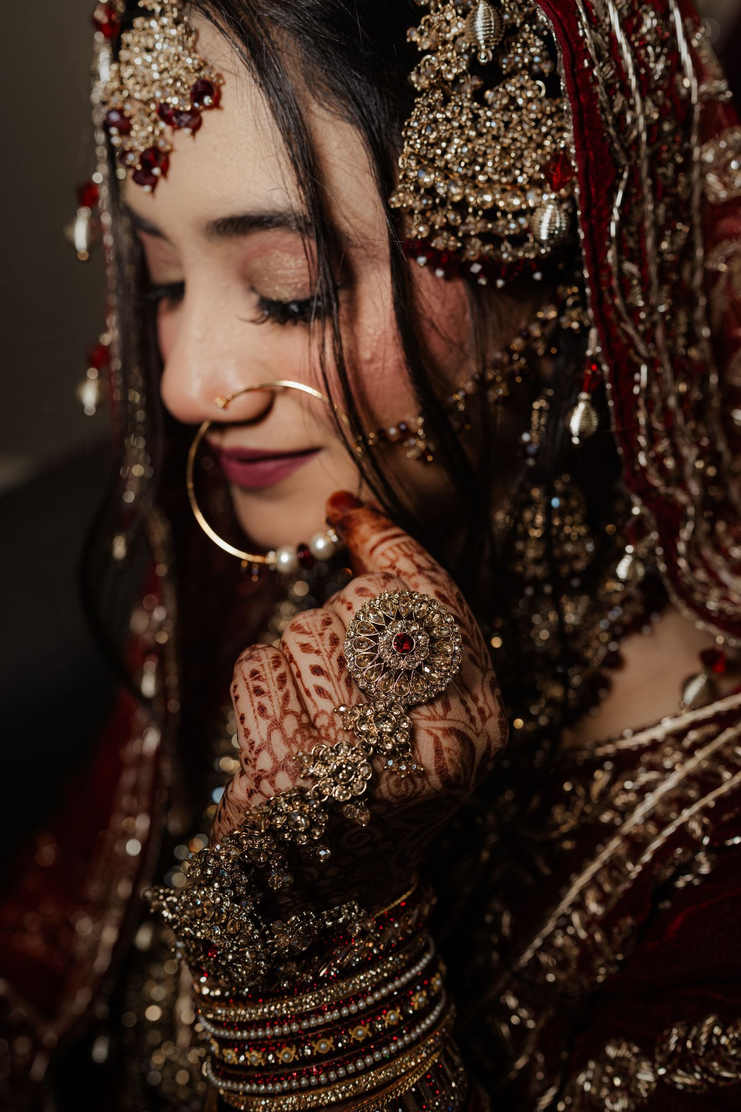 Close-up of South Asian bride with eyes closed wearing gold nose ring, bridal jewelry, and intricate henna mehndi.