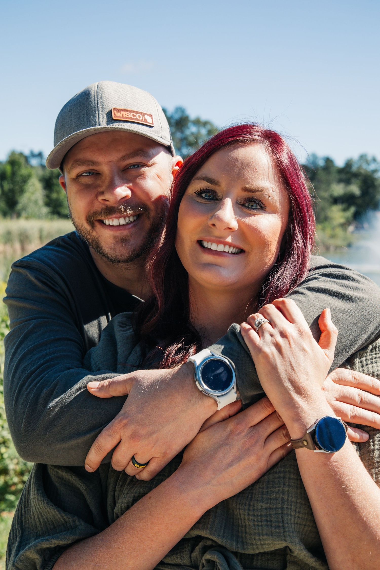 A couple shares a candid laughing moment together outdoors in a sunlit forest setting.