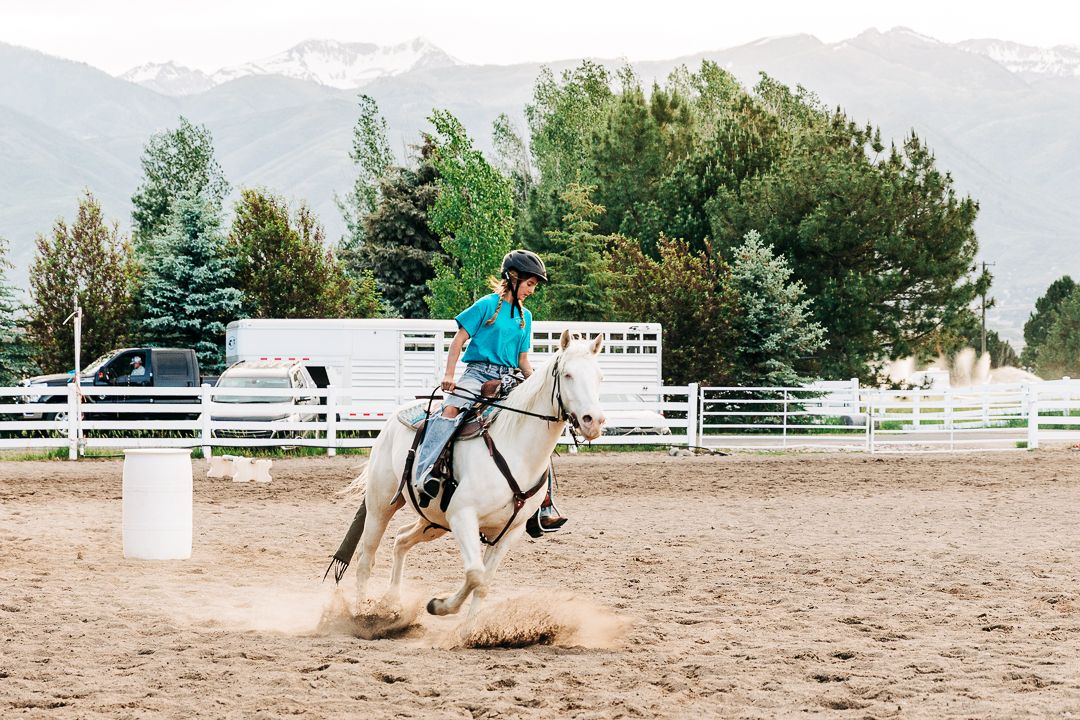 Equestrian riding in arena performs barrel racing maneuver with mountains in background.
