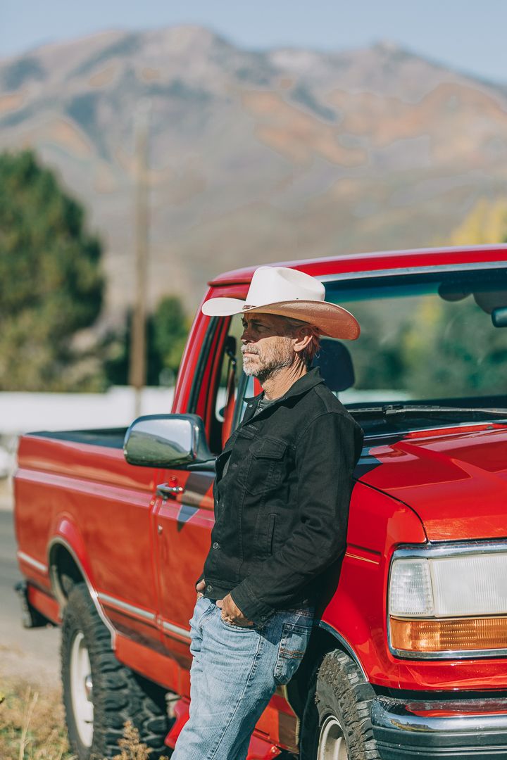 A red pickup truck parked in a rural mountain landscape with someone leaning against its side.