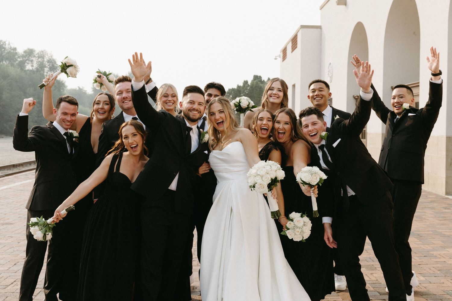 Wedding party celebrating with raised arms in formal black and white attire.
