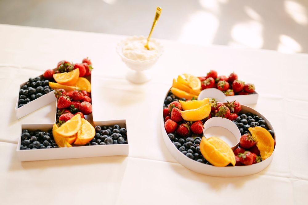 Number 16 shaped trays filled with fresh blueberries, strawberries, and orange slices on a white table.