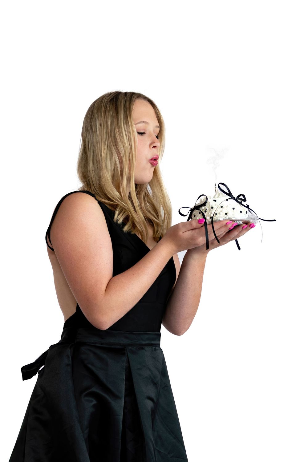 Blonde woman in black dress blowing out candles on a polka dot gift box with black ribbon bow.