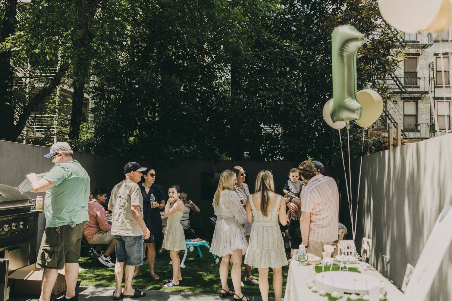 A small outdoor garden party celebration with balloons, decorations and guests mingling in white and beige attire.