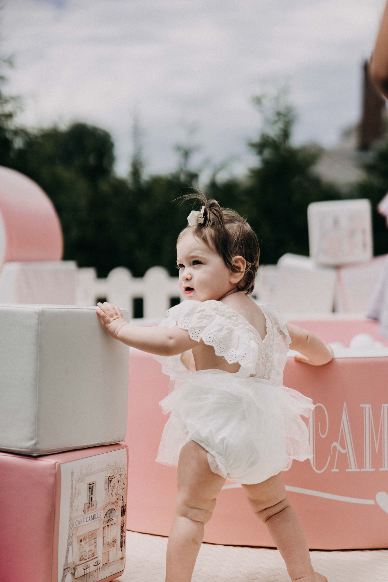 Baby in white tulle romper plays among pink and white party decorations.