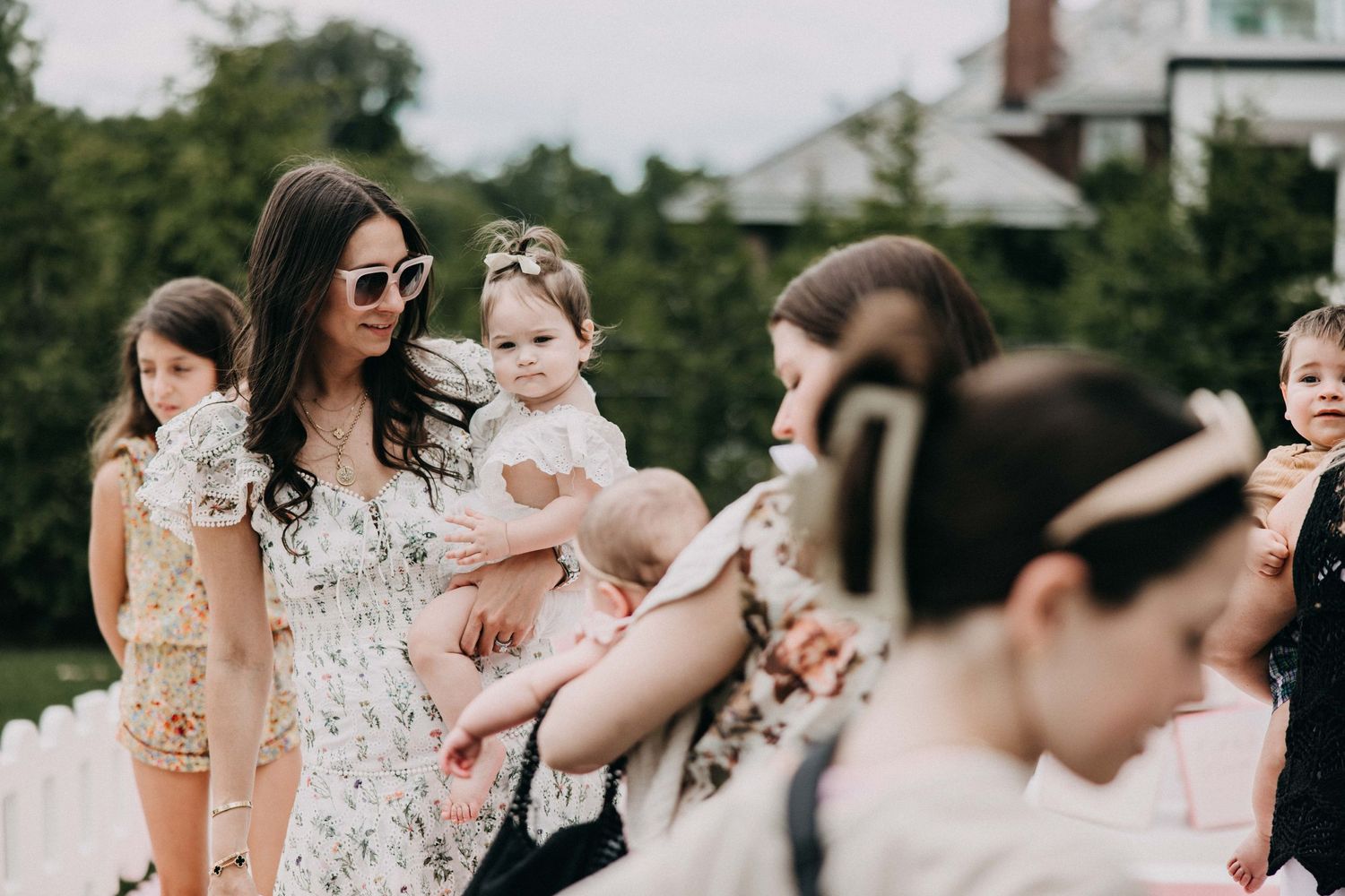 Outdoor party scene with guests mingling around decorative white fence and pink accents.
