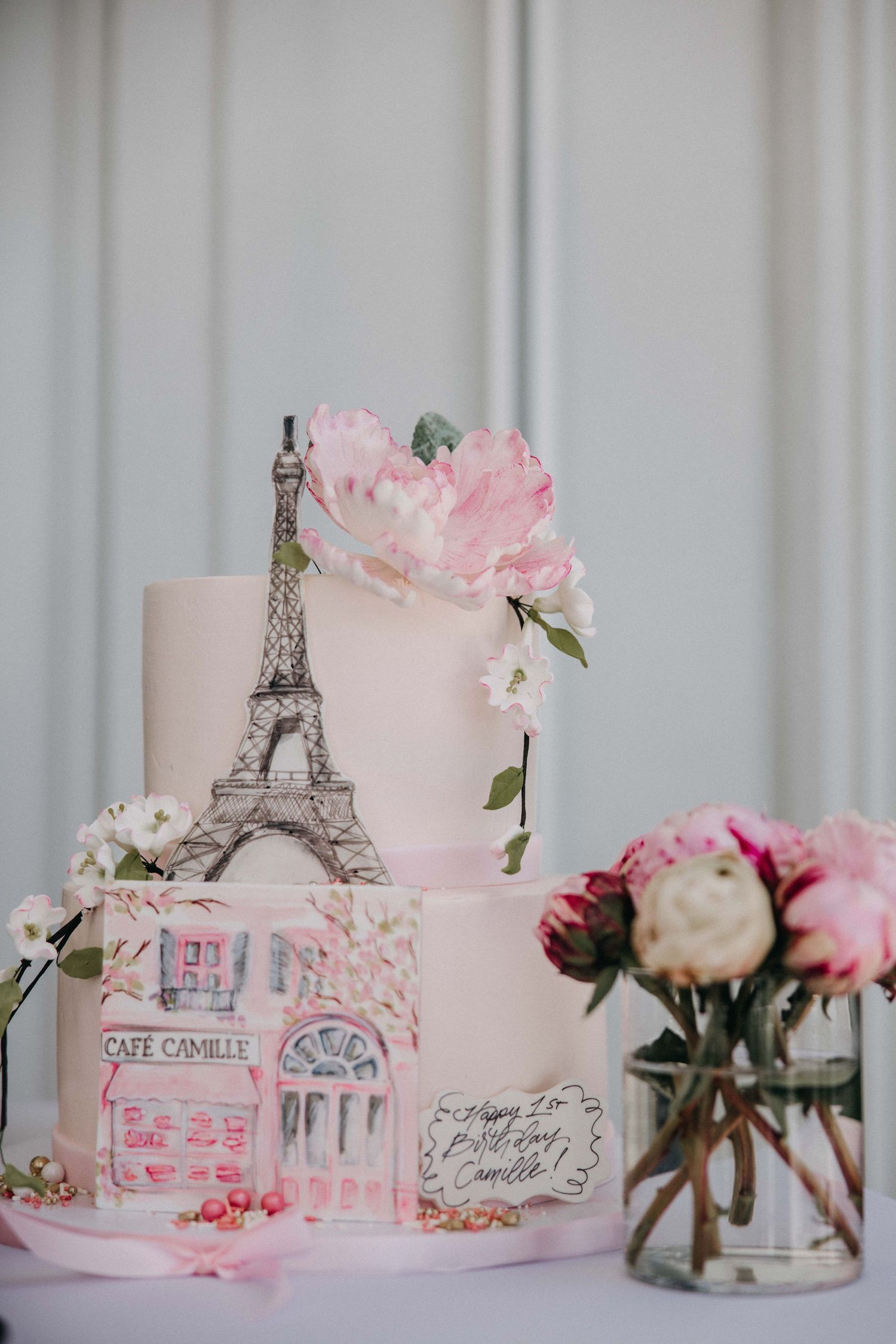 A pink Paris-themed cake with Eiffel Tower decoration and fresh flowers on display.