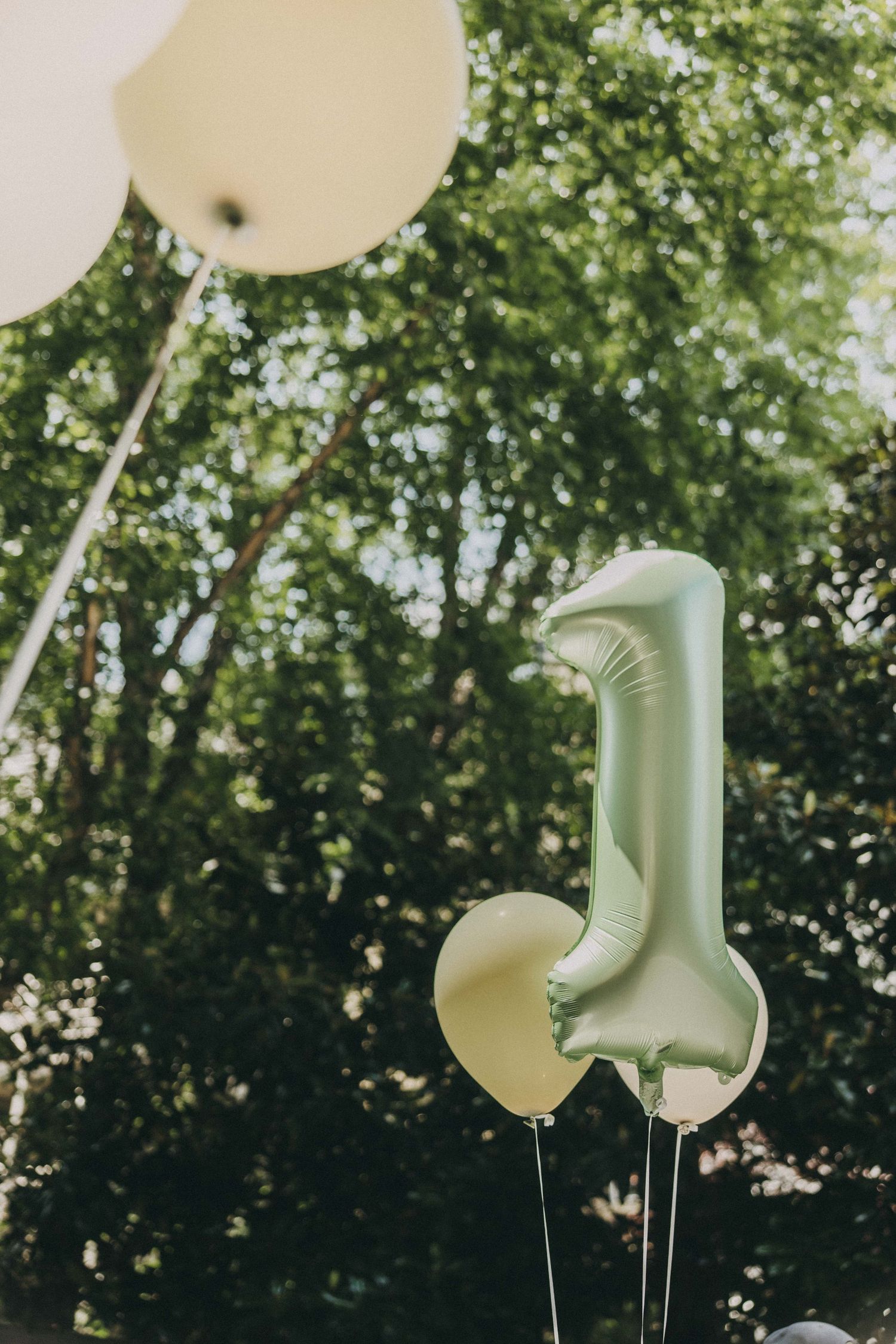 White balloons float against a leafy green backdrop creating an ethereal outdoor party atmosphere.