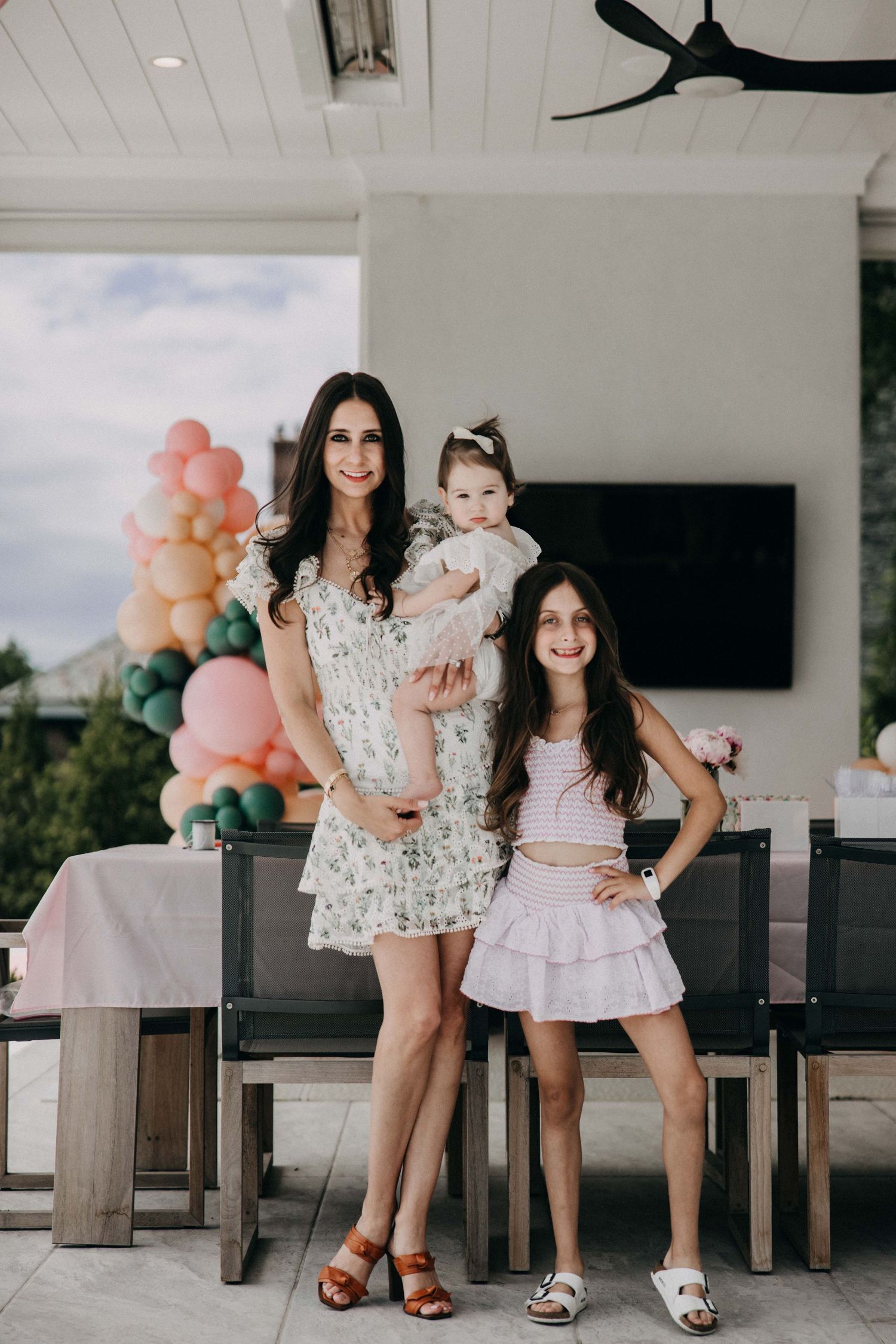 Family portrait at outdoor party with pink balloon arch and white table settings.