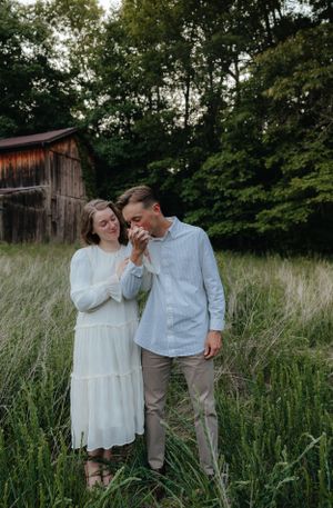 A couple shares joyful moments in a rustic field with an old barn in the background.