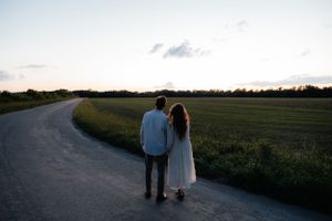 Silhouetted figures walking with their dog along a scenic country path at sunset.