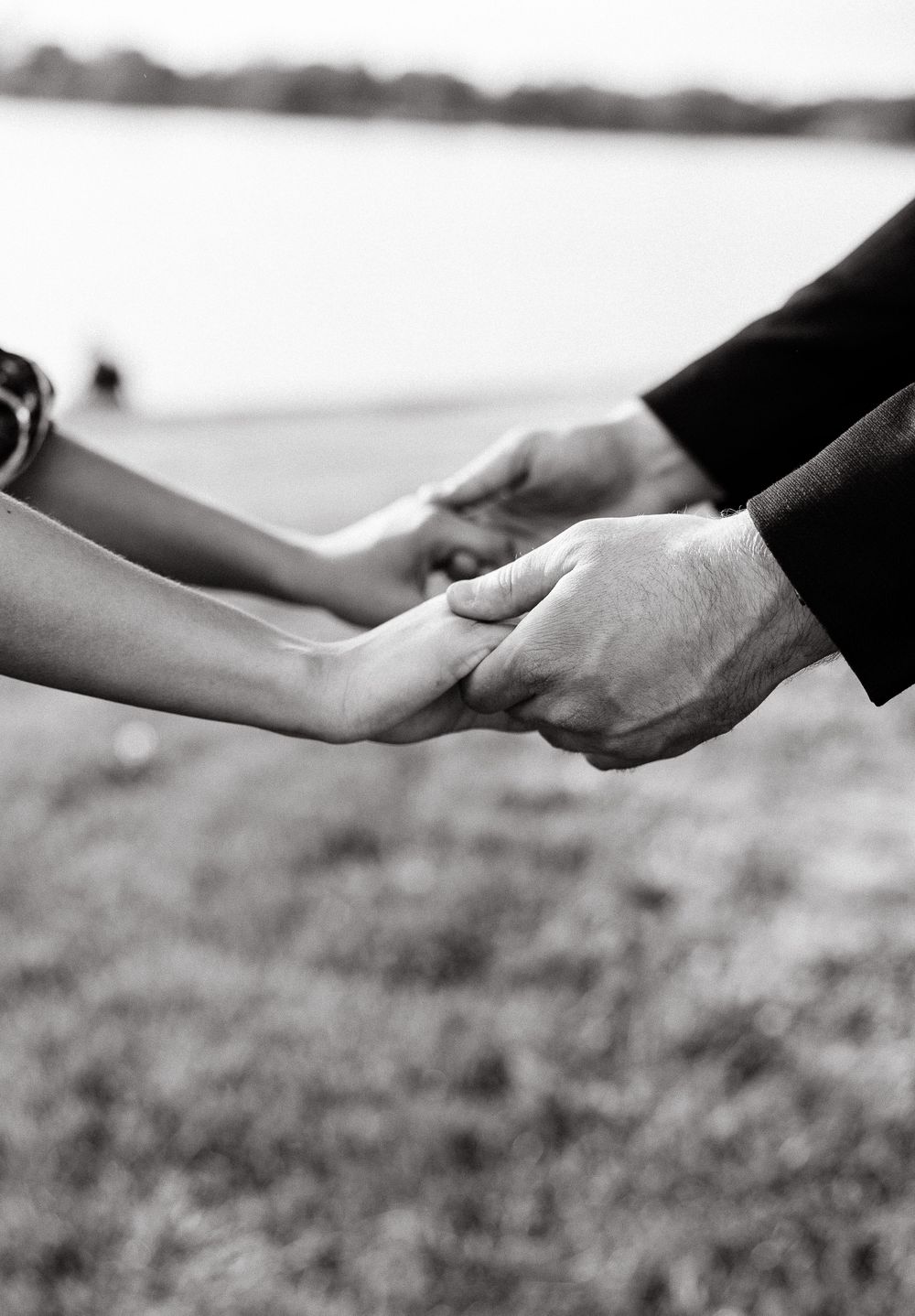 Close-up black and white photo of hands reaching out to hold each other against a blurred background.