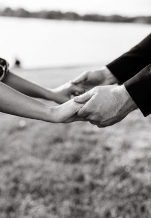 Close-up black and white photo of hands reaching out to hold each other against a blurred background.