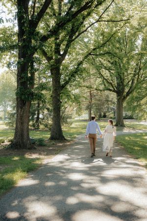 Tree-lined path with couple and dog walking in dappled sunlight.
