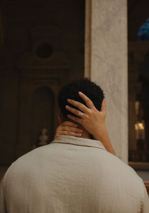 A person seen from behind with a hand resting on their neck inside an elegant marble interior.