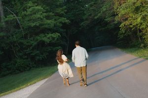 Couple walking hand in hand down a peaceful tree-lined road surrounded by lush green forest.