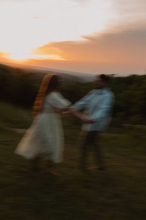 A couple dances together at sunset on a grassy hill, captured in a dreamy motion blur with warm golden sky.