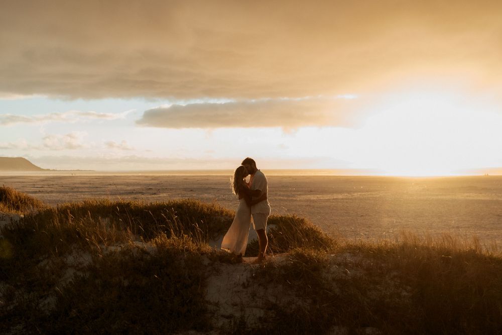 Romantic sunset silhouette captures a loving embrace on a hilltop overlooking a vast golden landscape at dusk.