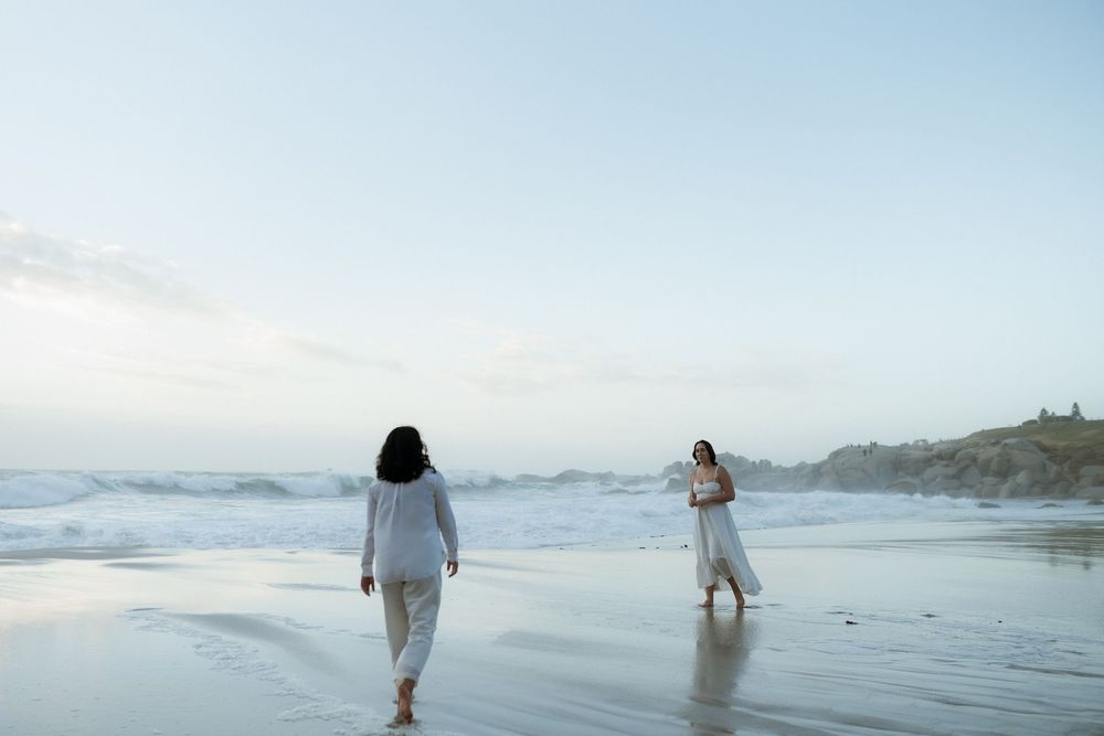 People walking along a misty beach shoreline at sunset with waves crashing on the sand.