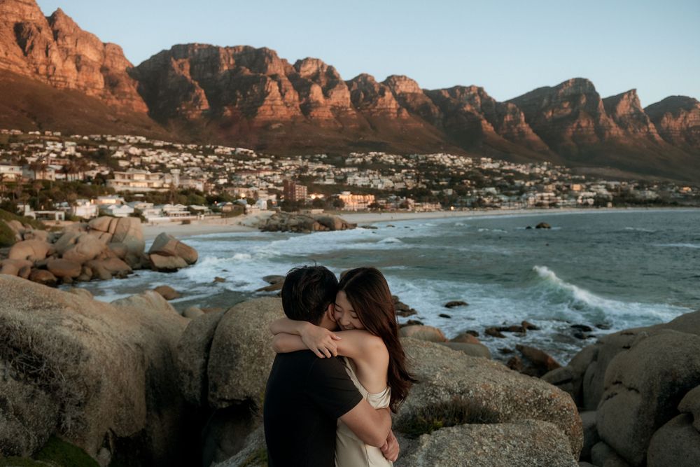 Scenic coastal landscape with rugged cliffs and mountains overlooking a serene beach at sunset.