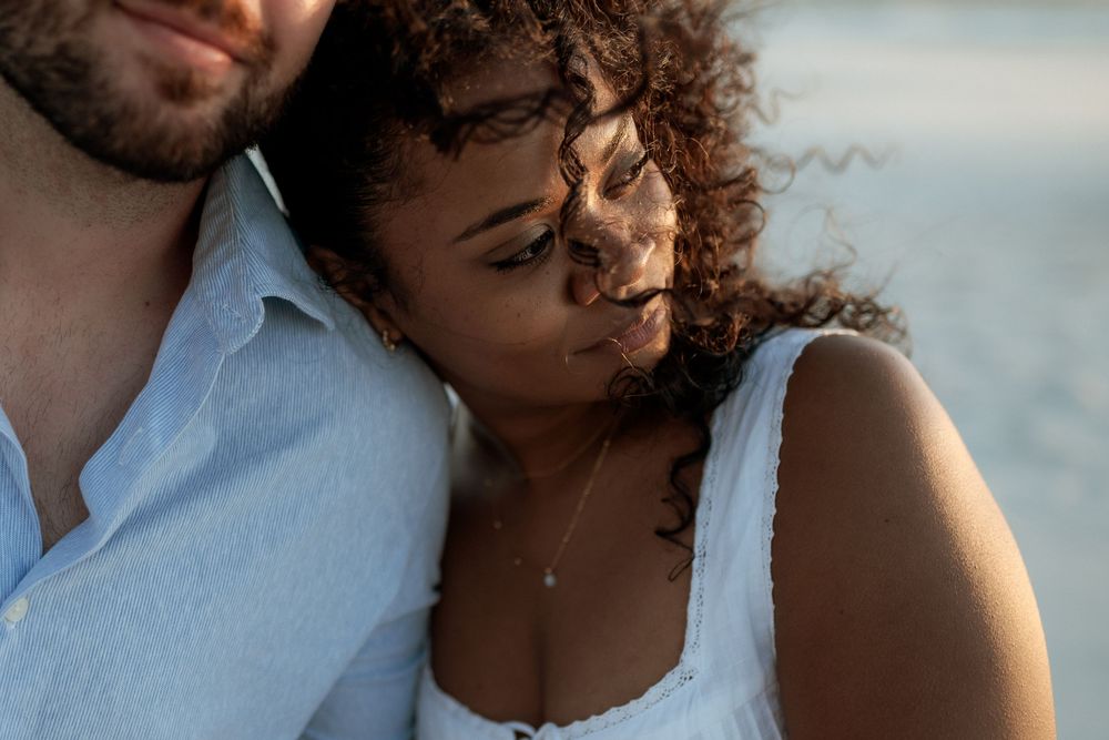 Close-up portrait of a couple in white clothing embracing during a romantic outdoor photoshoot at sunset.