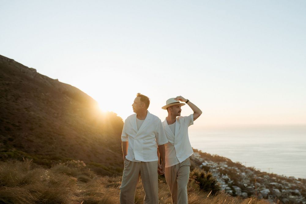 Two people stand on a coastal cliff at sunset overlooking the ocean in romantic silhouette.