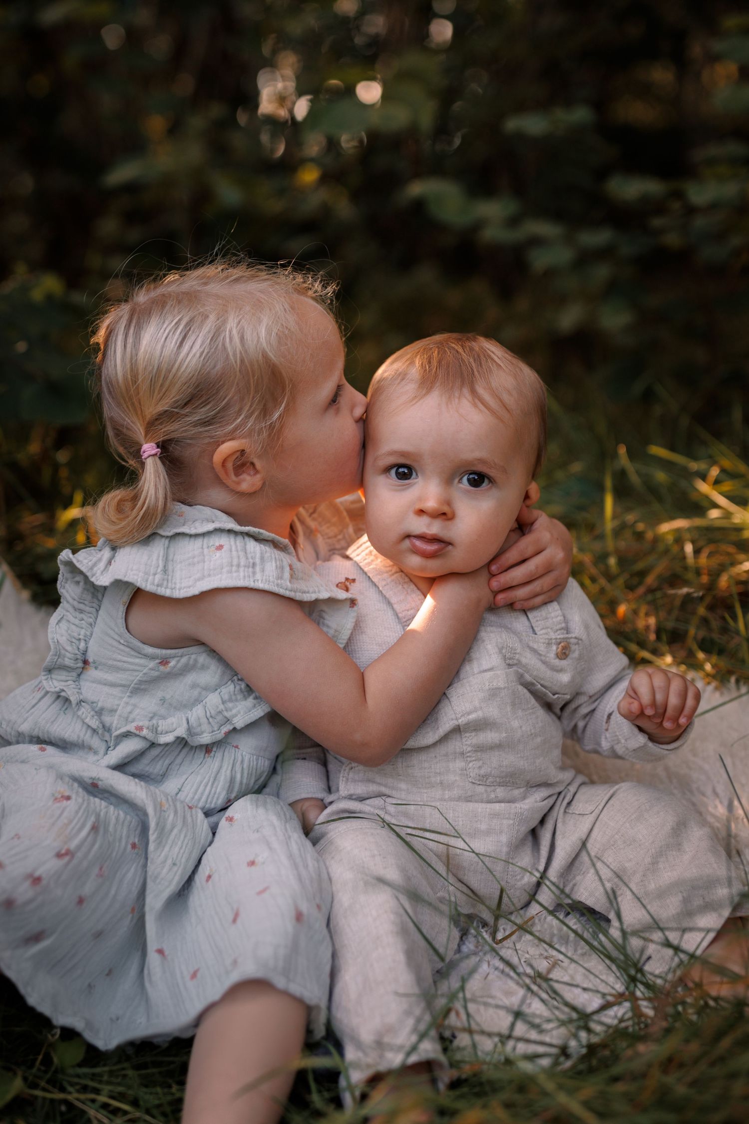 Sweet outdoor portrait of two young siblings in light colored outfits sharing a tender moment together in nature.