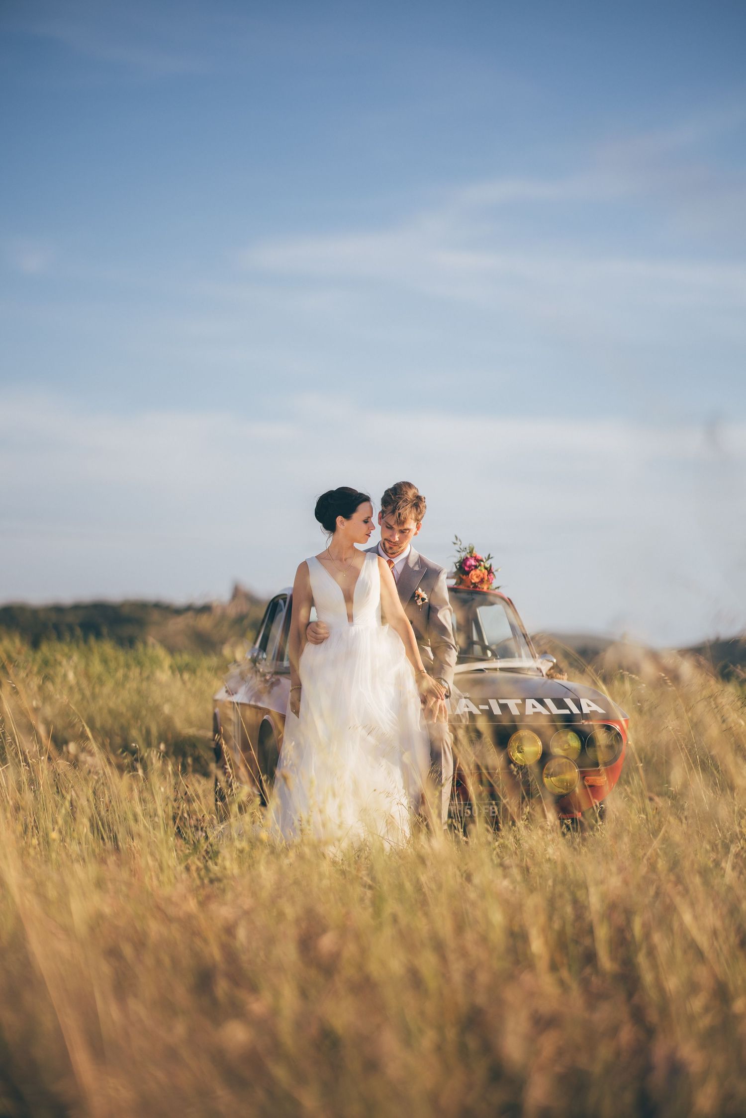Romantic wedding portrait with sun flare showing bride and groom under delicate veil in golden sunlight.