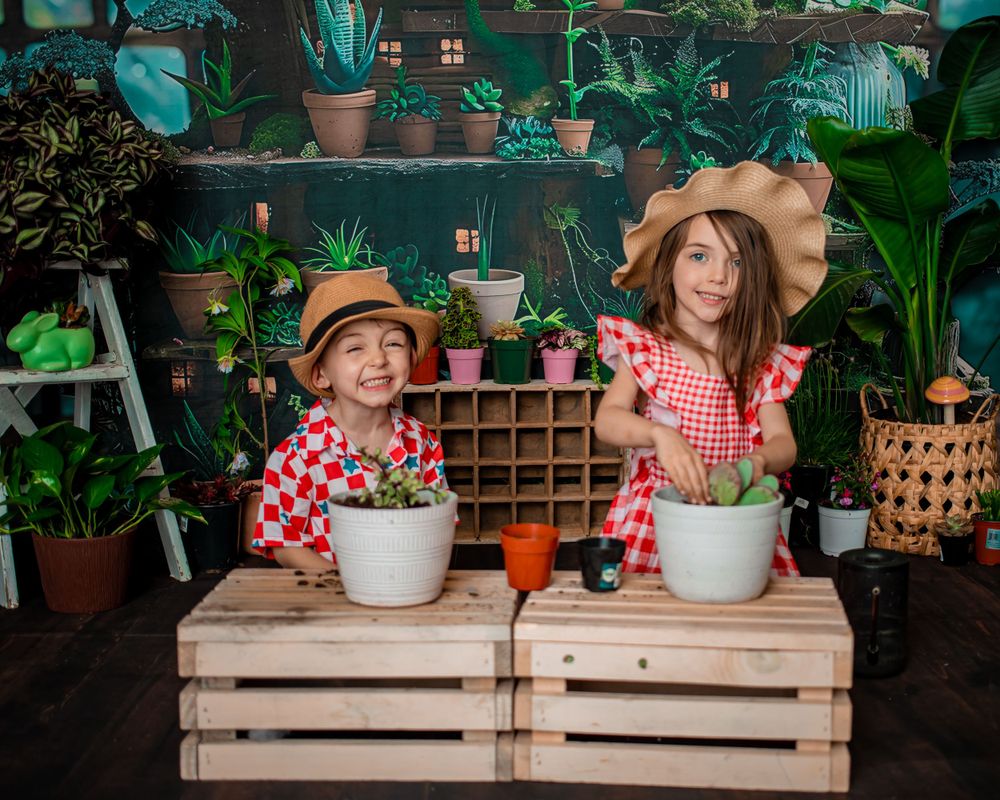 Two children gardening with potted plants on wooden crates in greenhouse setting.