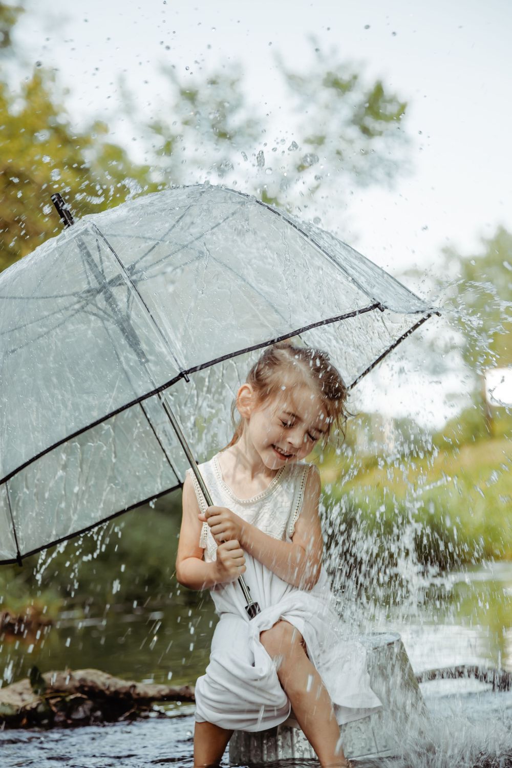 Child playing in the rain with a clear umbrella creating splashing water effects.