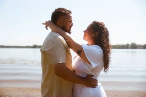 A couple embraces lovingly on a beach at sunset with water and horizon visible in the background.